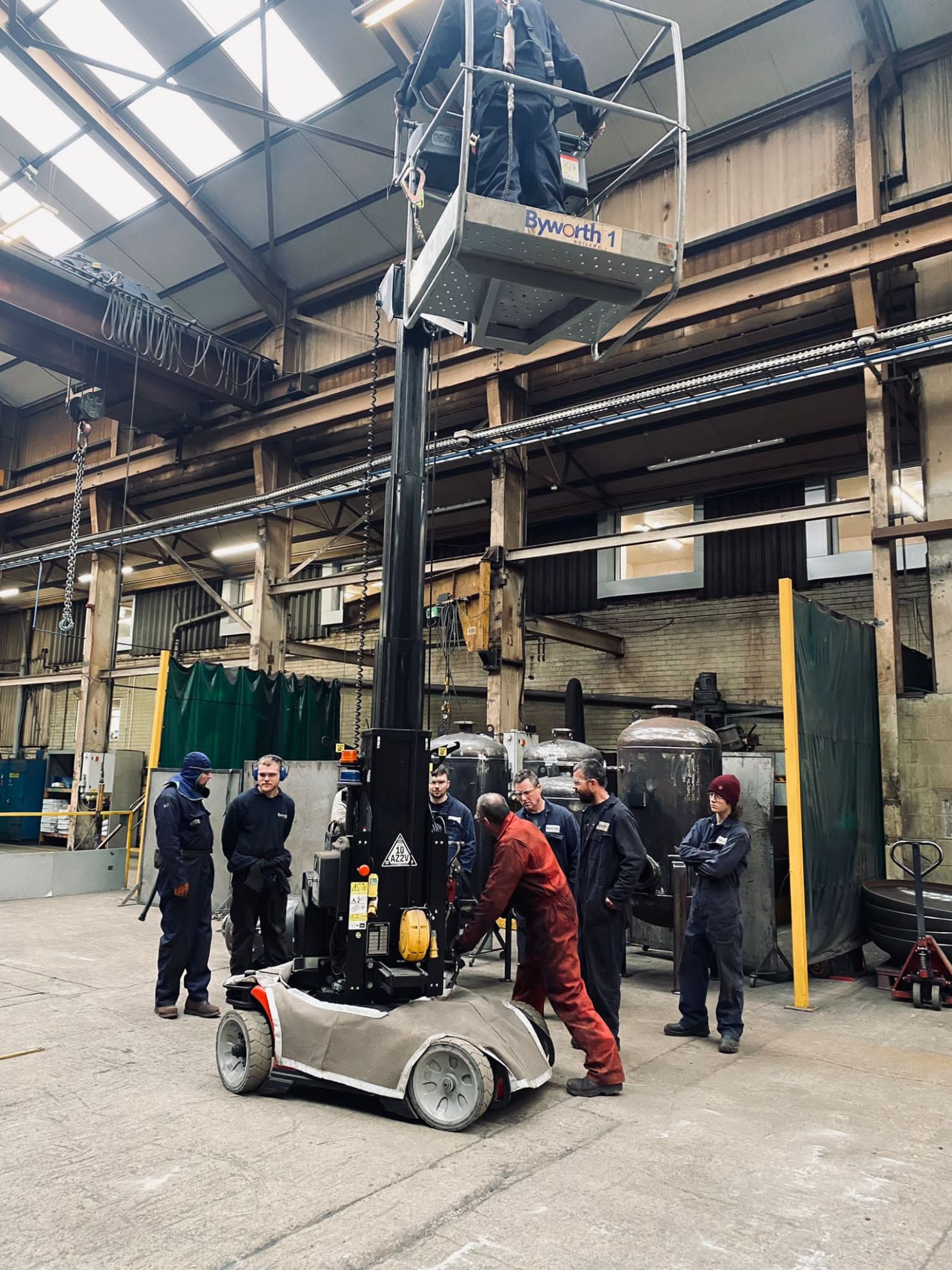 Mobile Elevating Work Platforms in action on a factory floor with a group of men in boiler suits listening to instructions