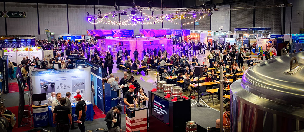 Trade show hall photographed from above, the show is buzzing with people and there are signs and beer pumps