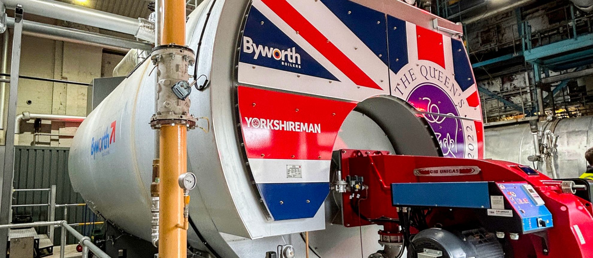 Large industrial boiler with a union jack on the front within a busy industrial boiler house 