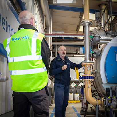 A man within an industrial boiler house talking to a second man wearing a high visibility vest